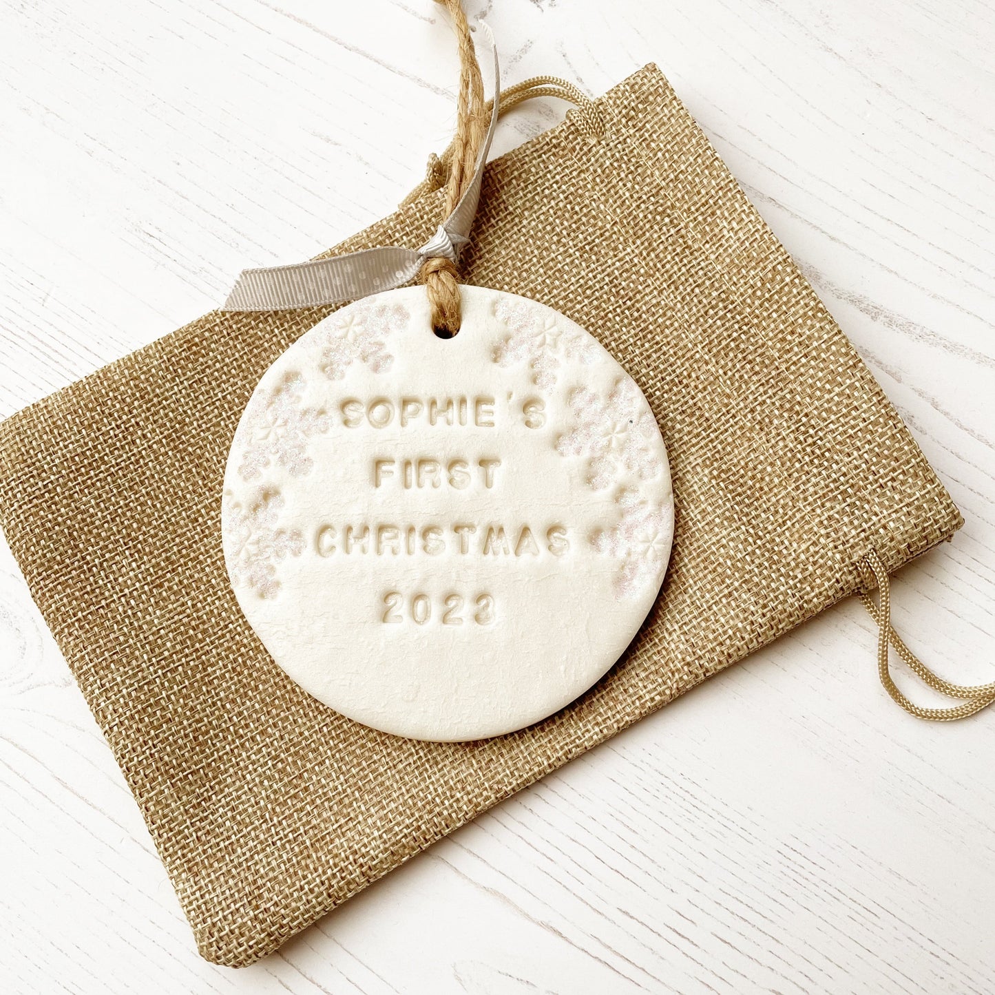 Personalised baby’s first Christmas bauble ornament, pearlised white round clay with SOPHIE’S FIRST CHRISTMAS 2023 (letters not painted), decorated with 3 iridescent glitter snowflakes on either side of the bauble