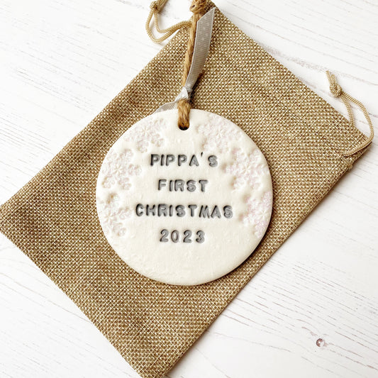 Personalised baby's first Christmas bauble ornament, pearlised white round clay with PIPPA’S FIRST CHRISTMAS 2023 in grey paint, decorated with 3 iridescent glitter snowflakes on either side of the bauble