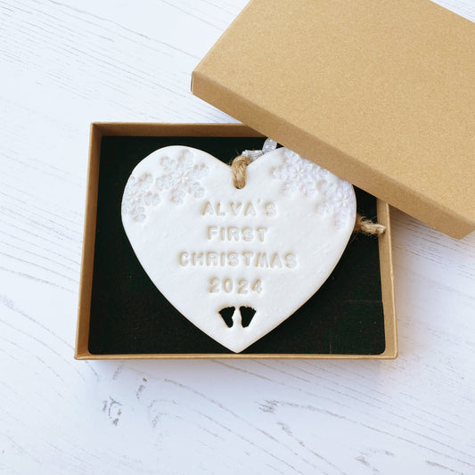 Personalised baby’s first Christmas heart ornament, pearlised white clay with ALVA’S FIRST CHRISTMAS 2024, decorated with 2 iridescent glitter snowflakes on either side of the top of the heart and baby feet cut out at the bottom