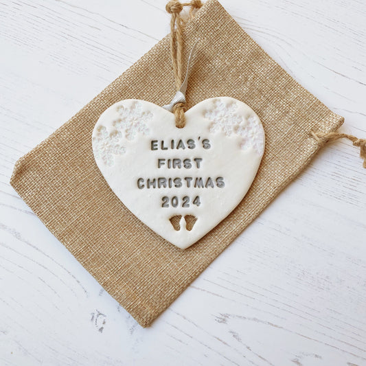 Personalised baby’s first Christmas heart ornament, pearlised white clay with ELIAS’S FIRST CHRISTMAS 2024 painted grey, decorated with 2 iridescent glitter snowflakes on either side of the top of the heart and baby feet cut out at the bottom