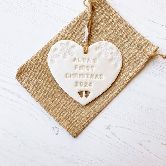 Personalised baby’s first Christmas heart ornament, pearlised white clay with ALVA’S FIRST CHRISTMAS 2024, decorated with 2 iridescent glitter snowflakes on either side of the top of the heart and baby feet cut out at the bottom