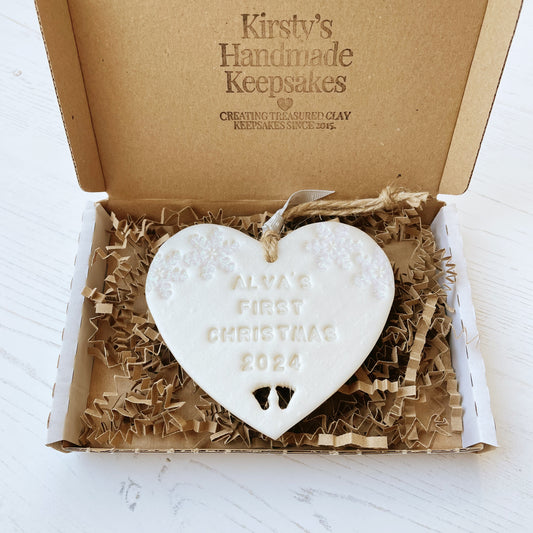 Personalised baby’s first Christmas heart ornament, pearlised white clay with ALVA’S FIRST CHRISTMAS 2024, decorated with 2 iridescent glitter snowflakes on either side of the top of the heart and baby feet cut out at the bottom