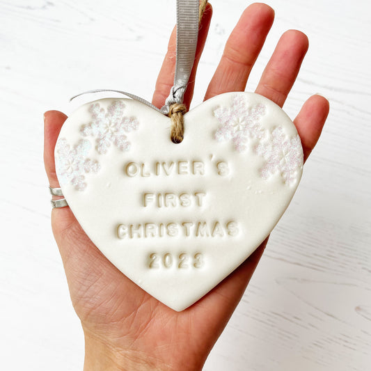 Personalised baby's first Christmas heart ornament, pearlised white clay with OLIVER’S FIRST CHRISTMAS 2023 (text not painted), decorated with 2 iridescent glitter snowflakes on either side of the top of the heart