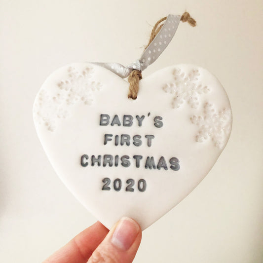 Baby’s first Christmas heart ornament, pearlised white clay with BABY’S FIRST CHRISTMAS 2020 painted grey, decorated with 2 iridescent glitter snowflakes on either side of the top of the heart