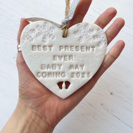 Personalised baby reveal Christmas heart ornament, pearlised white clay with BEST PRESENT EVER! BABY MAY COMING 2025, decorated with 2 iridescent glitter snowflakes on either side of the top of the heart