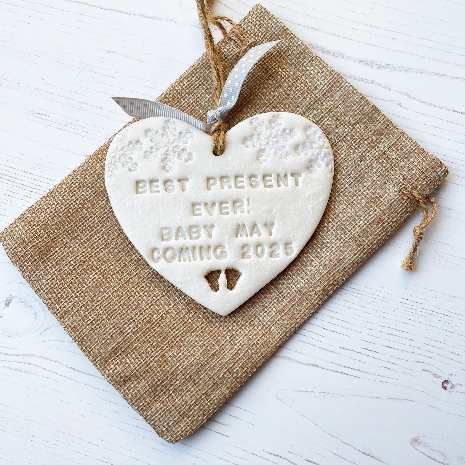 Personalised baby reveal Christmas heart ornament, pearlised white clay with BEST PRESENT EVER! BABY MAY COMING 2025, decorated with 2 iridescent glitter snowflakes on either side of the top of the heart