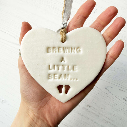 Personalised baby reveal gift, pearlised white clay heart with feet cut out of the bottom personalised with BREWING A LITTLE BEAN…