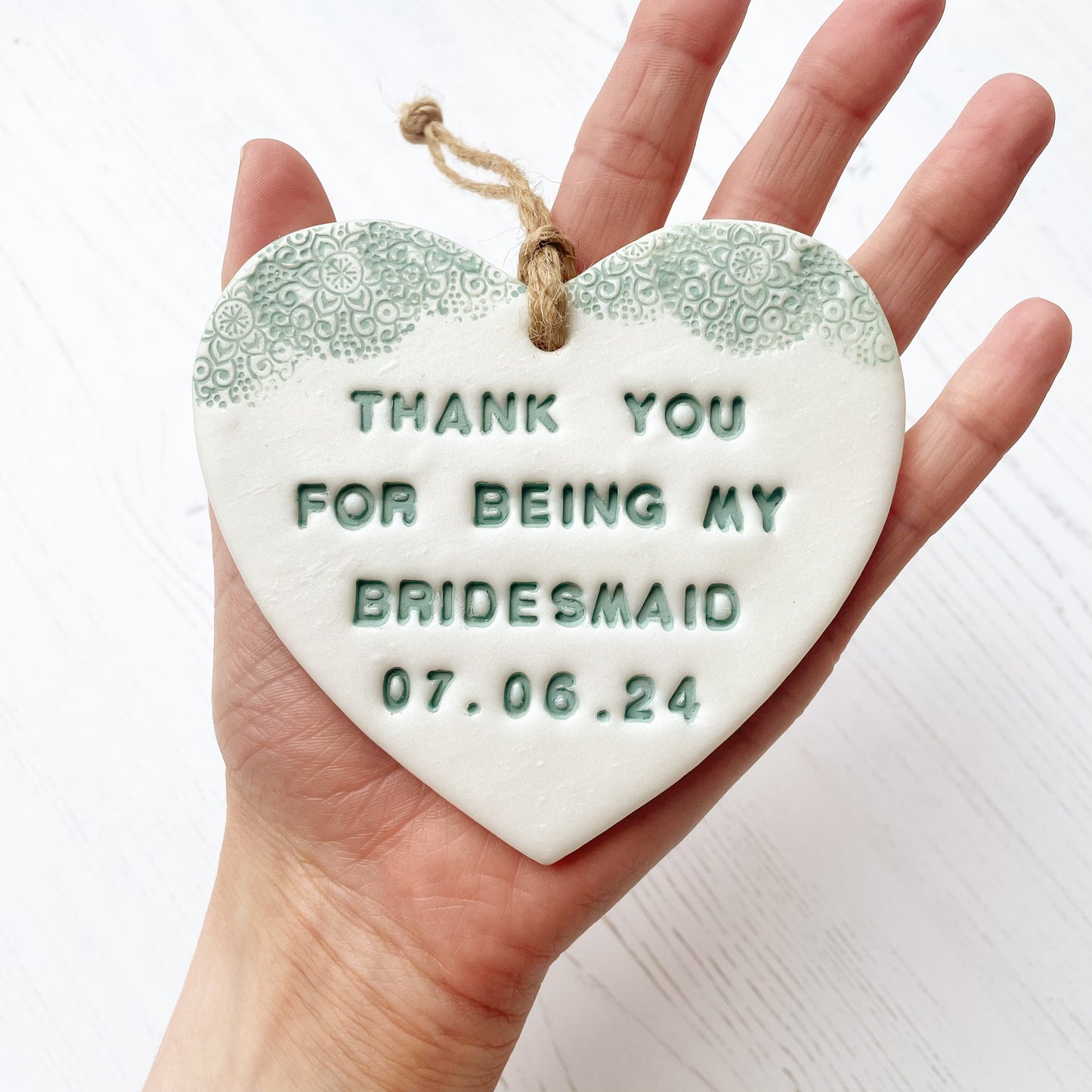 Personalised Bridesmaid thank you gift, pearlised white clay hanging heart with a sage green lace edge at the top of the heart, the heart is personalised with THANK YOU FOR BEING MY BRIDESMAID 07.06.24