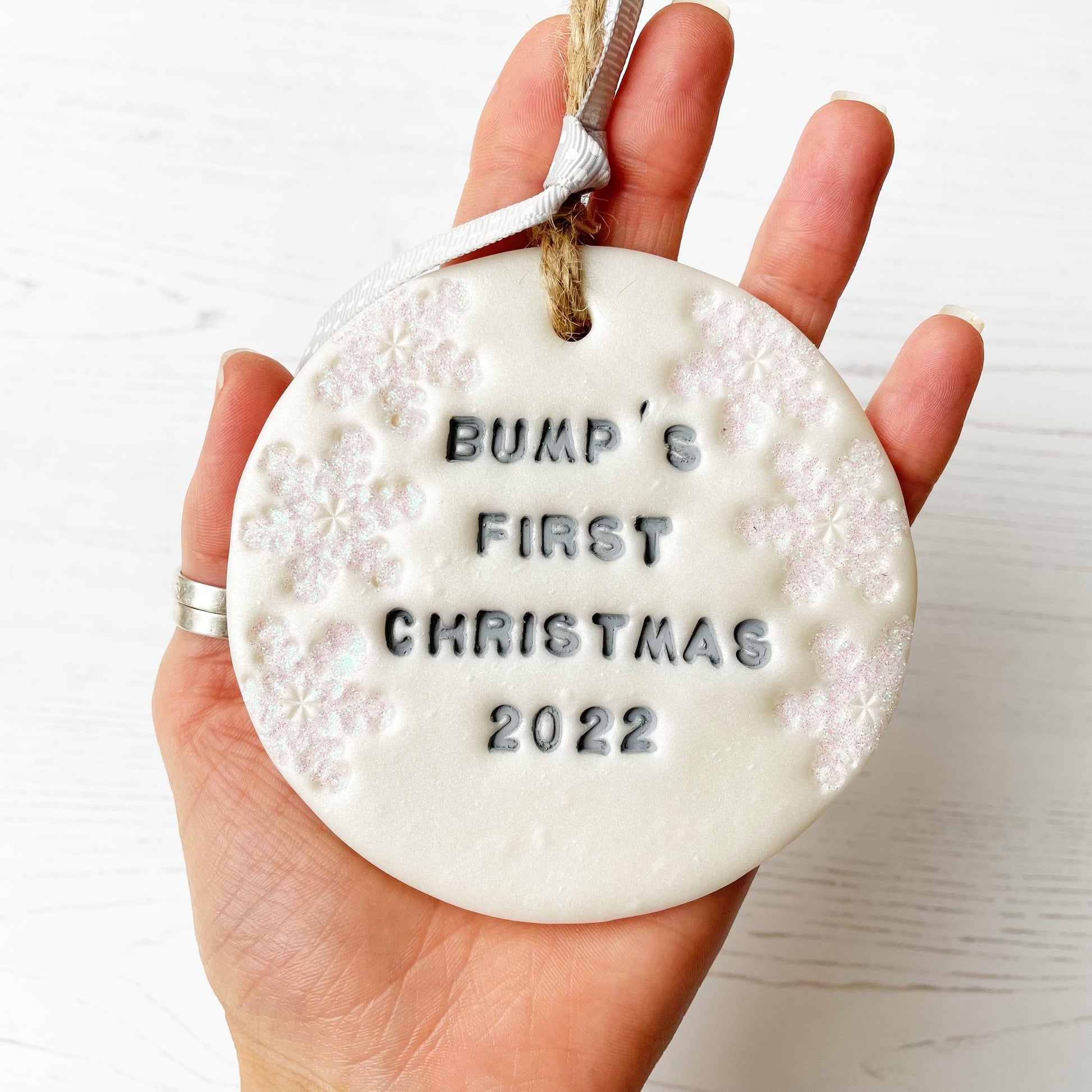 Personalised baby's first Christmas bauble ornament, pearlised white round clay with BUMP’S FIRST CHRISTMAS 2022 in grey paint, decorated with 3 iridescent glitter snowflakes on either side of the bauble