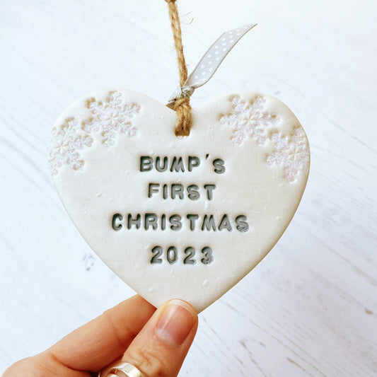 Personalised bump's first Christmas heart ornament, pearlised white clay with BUMP'S FIRST CHRISTMAS 2023 painted grey, decorated with 2 iridescent glitter snowflakes on either side of the top of the heart