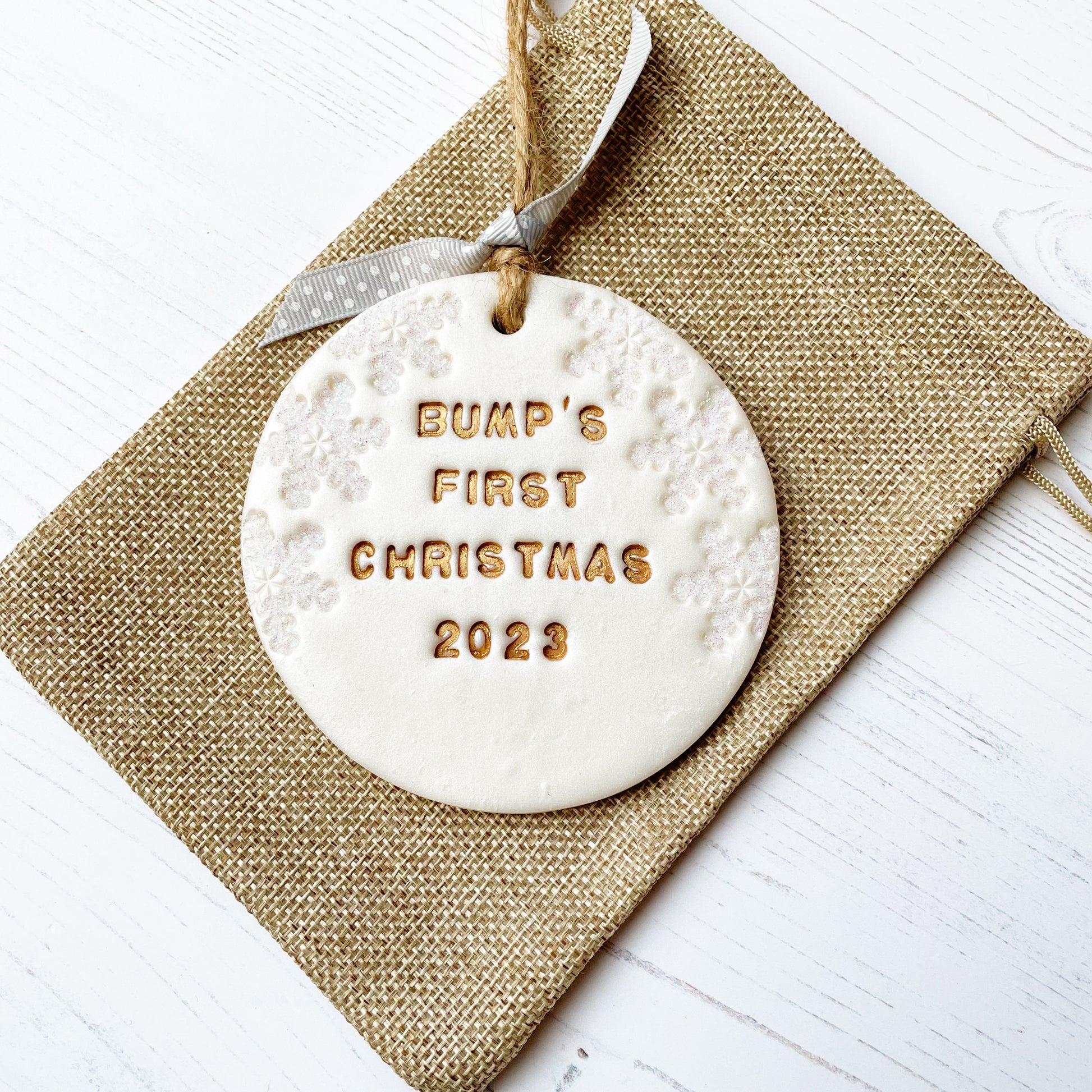 Personalised bump's first Christmas bauble ornament, pearlised white round clay with BUMP’S FIRST CHRISTMAS 2023 in gold paint, decorated with 3 iridescent glitter snowflakes on either side of the bauble