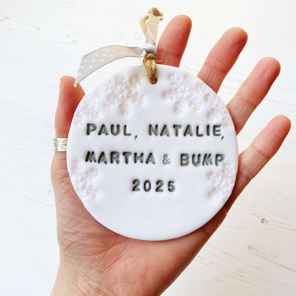 Personalised bump’s first Christmas bauble ornament, glitter white round clay with PAUL, NATALIE, MARTHA & BUMP 2025 in grey paint, decorated with 3 iridescent glitter snowflakes on either side of the bauble