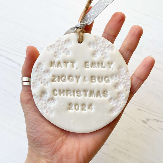 Personalised bump’s first Christmas bauble ornament, pearlised white round clay with MATT, EMILY, ZIGGY & BUG CHRISTMAS 2024, decorated with 3 iridescent glitter snowflakes on either side of the bauble