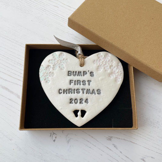 Personalised bump’s first Christmas heart ornament, pearlised white clay with BUMP’S FIRST CHRISTMAS 2024 painted grey, decorated with 2 iridescent glitter snowflakes on either side of the top of the heart and baby feet cut out at the bottom