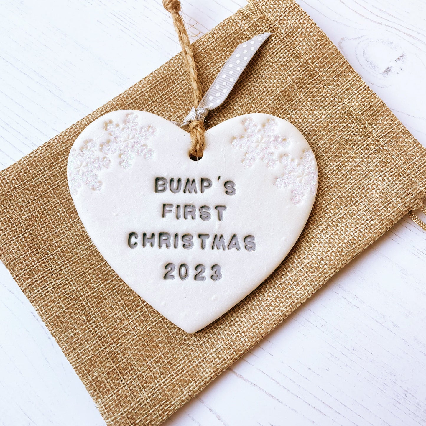 Personalised bump's first Christmas heart ornament, pearlised white clay with BUMP'S FIRST CHRISTMAS 2023 painted grey, decorated with 2 iridescent glitter snowflakes on either side of the top of the heart