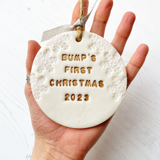 Personalised bump's first Christmas bauble ornament, pearlised white round clay with BUMP’S FIRST CHRISTMAS 2023 in gold paint, decorated with 3 iridescent glitter snowflakes on either side of the bauble