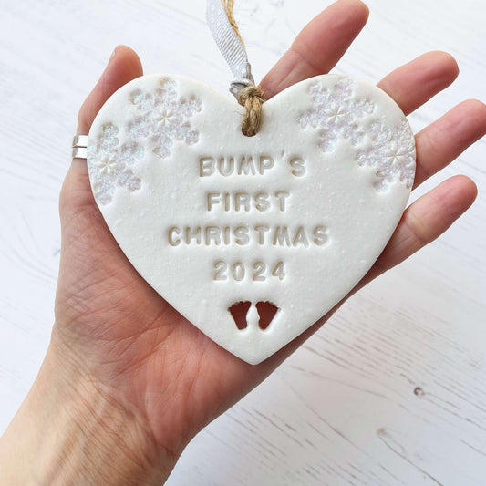 Personalised baby’s first Christmas heart ornament, pearlised white clay with ALVA’S FIRST CHRISTMAS 2024, decorated with 2 iridescent glitter snowflakes on either side of the top of the heart and baby feet cut out at the bottom