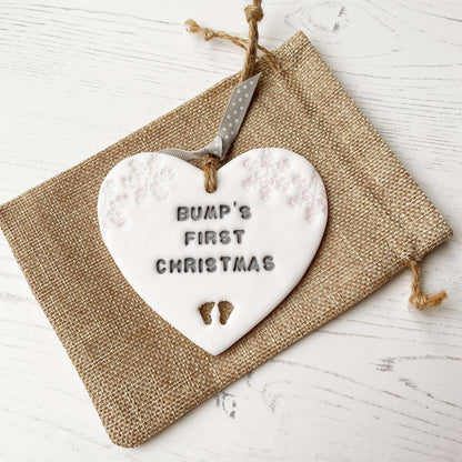 Personalised bump’s first Christmas heart ornament, glitter white clay with BUMP’S FIRST CHRISTMAS painted grey, decorated with 2 iridescent glitter snowflakes on either side of the top of the heart and baby feet cut out at the bottom