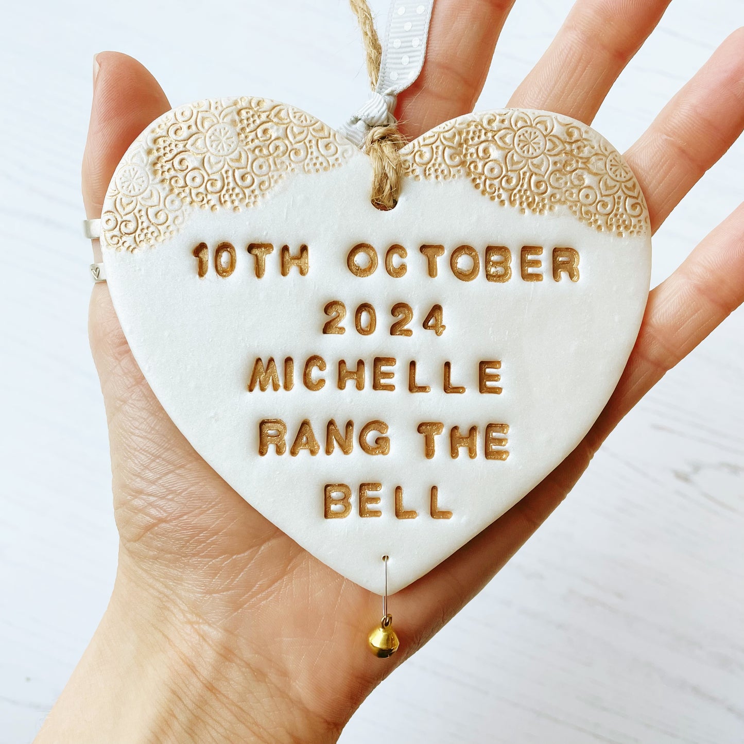 Personalised cancer survivor gift pearlised white clay hanging heart with gold lace edge at the top and a gold bell hanging below personalised with 10th OCTOBER 2024 MICHELLE RANG THE BELL