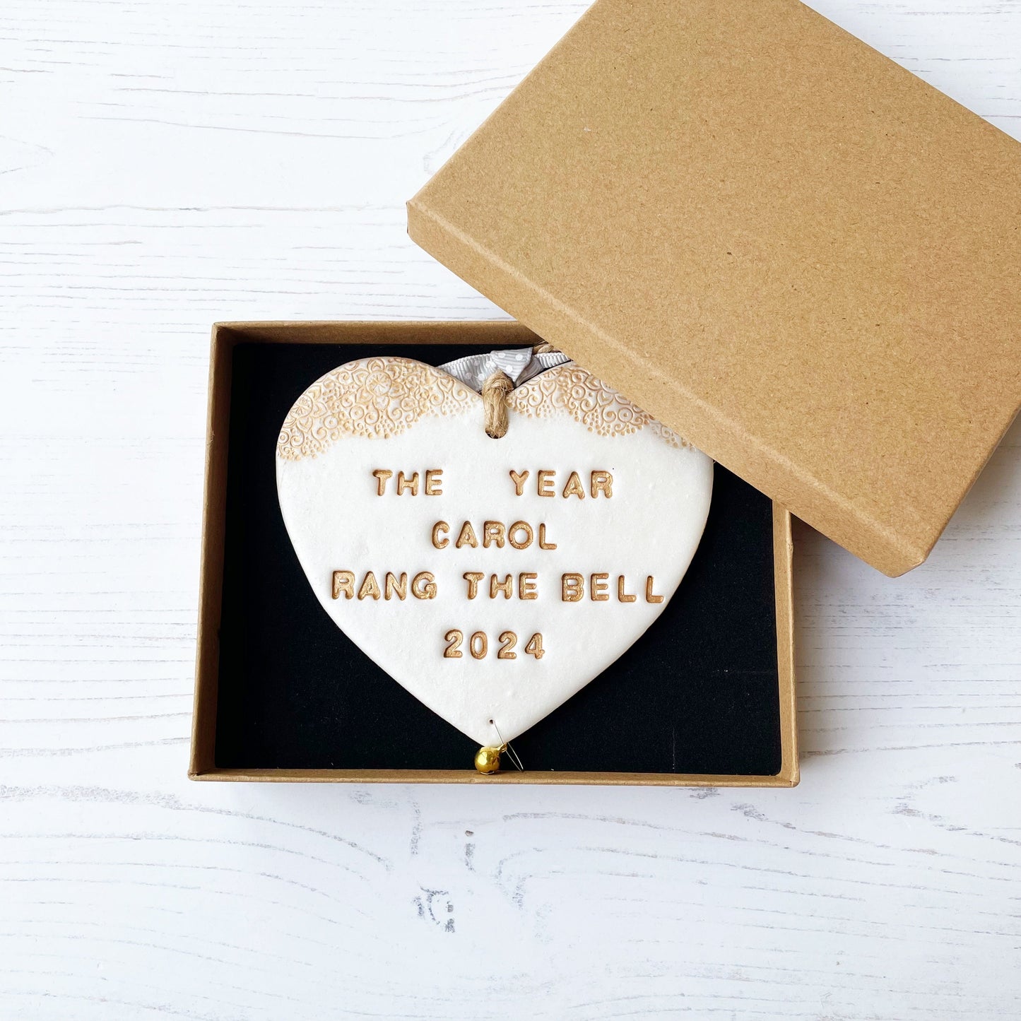 Personalised cancer survivor gift, pearlised white clay hanging heart with a gold lace edge at the top of the heart and a gold bell hanging below, the heart is personalised with THE YEAR CAROL RANG THE BELL 2024. In a luxury Kraft brown gift box