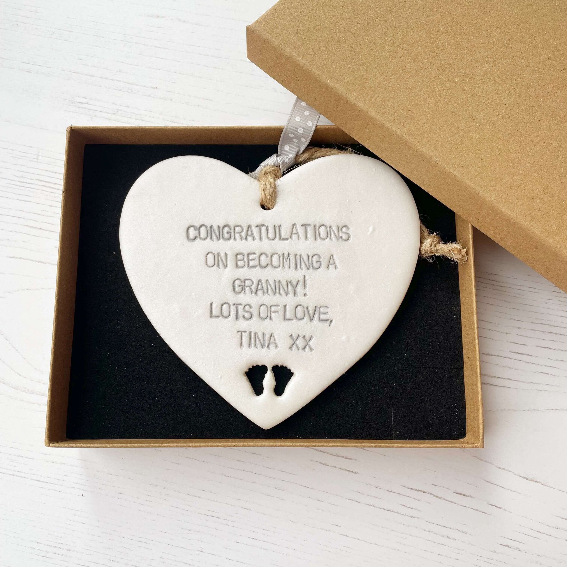 Pearlised white clay hanging heart with baby feet cut out of the bottom and grey personalisation, the heart is personalised with CONGRATULATIONS ON BECOMING A GRANNY! LOTS OF LOVE TINA XX