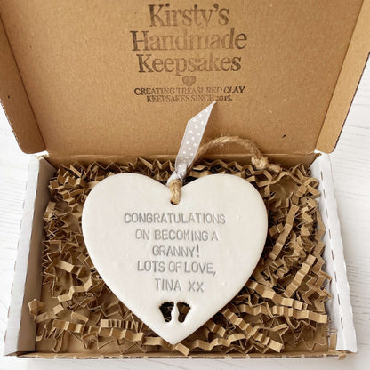 Pearlised white clay hanging heart with baby feet cut out of the bottom and grey personalisation, the heart is personalised with CONGRATULATIONS ON BECOMING A GRANNY! LOTS OF LOVE TINA XX