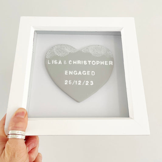 Personalised framed engagement gift, grey clay heart with a white lace edge at the top of the heart in a white box frame, the heart is personalised with LISA & CHRISTOPHER D 25/12/23