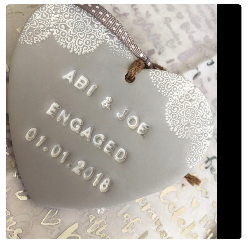 A grey polymer clay heart  ornament hand stamped with 'ABI & JOE ENGAGED 01.01.2018