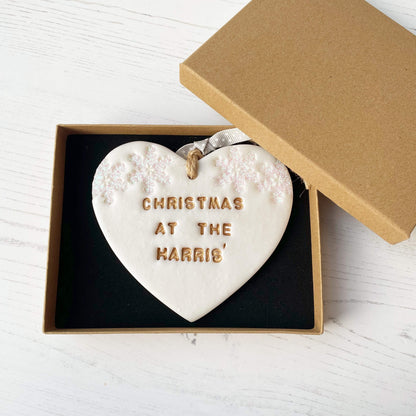 Personalised family Christmas heart ornament, pearlised white clay with CHRISTMAS AT THE HARRIS’ painted gold, decorated with 2 iridescent glitter snowflakes on either side of the top of the heart
