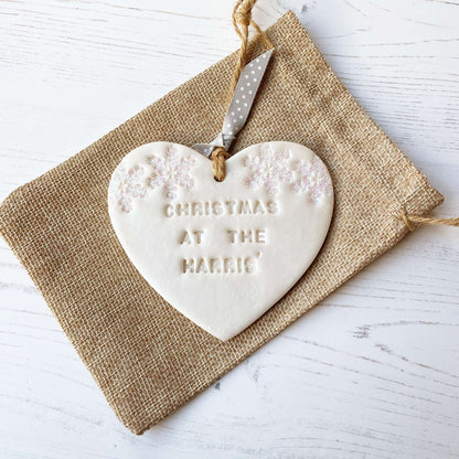 Personalised family Christmas heart ornament, pearlised white clay with CHRISTMAS AT THE HARRIS’ (text not painted), decorated with 2 iridescent glitter snowflakes on either side of the top of the heart