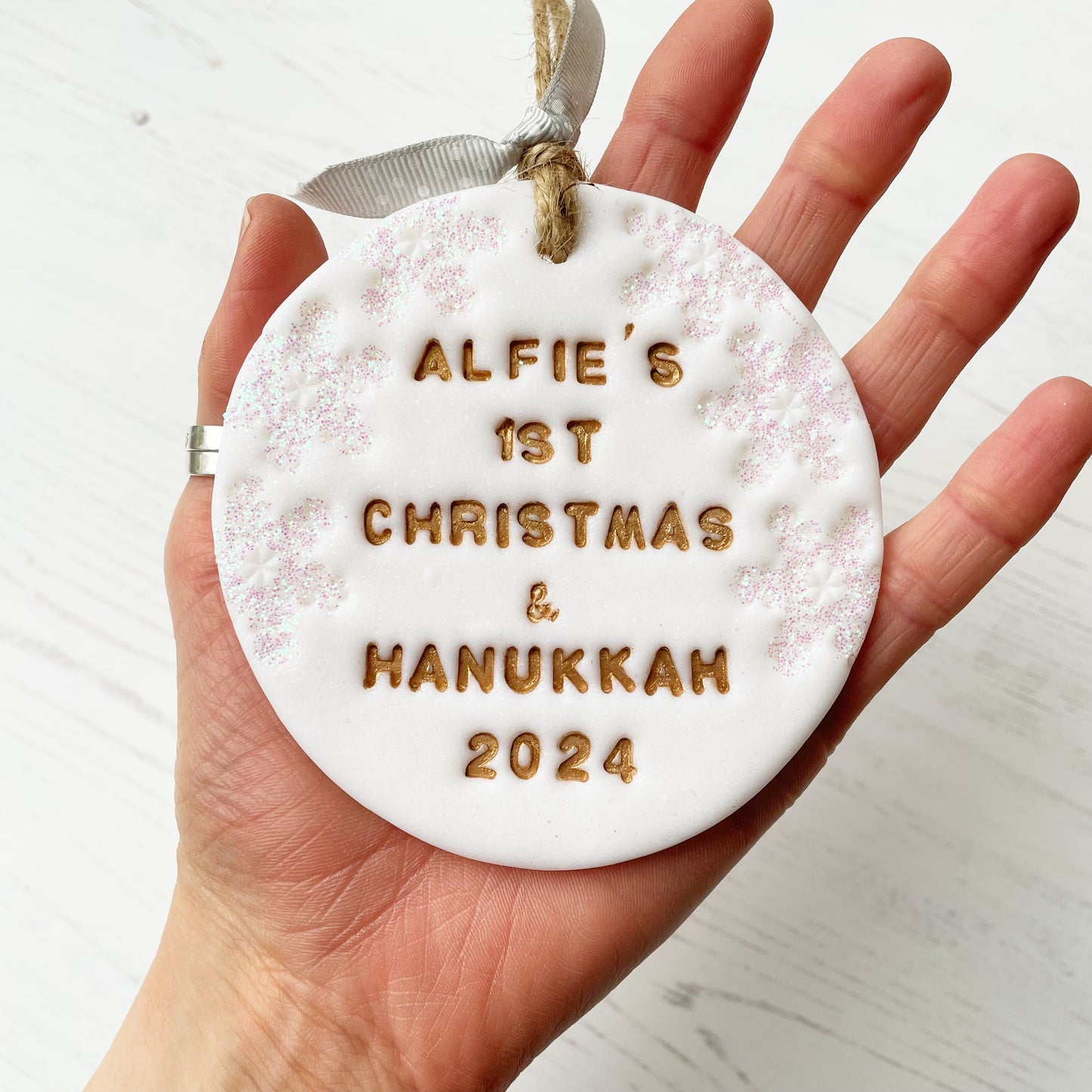 Personalised baby’s first Christmas and Hanukkah bauble ornament, glitter white clay round personalised with ALFIE’S FIRST CHRISTMAS & HANUKKAH 2024 in gold paint, decorated with 3 iridescent glitter snowflakes on either side of the bauble