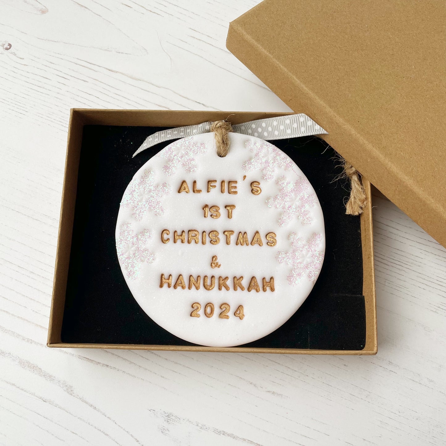 Personalised baby’s first Christmas and Hanukkah bauble ornament, glitter white clay round personalised with ALFIE’S FIRST CHRISTMAS & HANUKKAH 2024 in gold paint, decorated with 3 iridescent glitter snowflakes on either side of the bauble