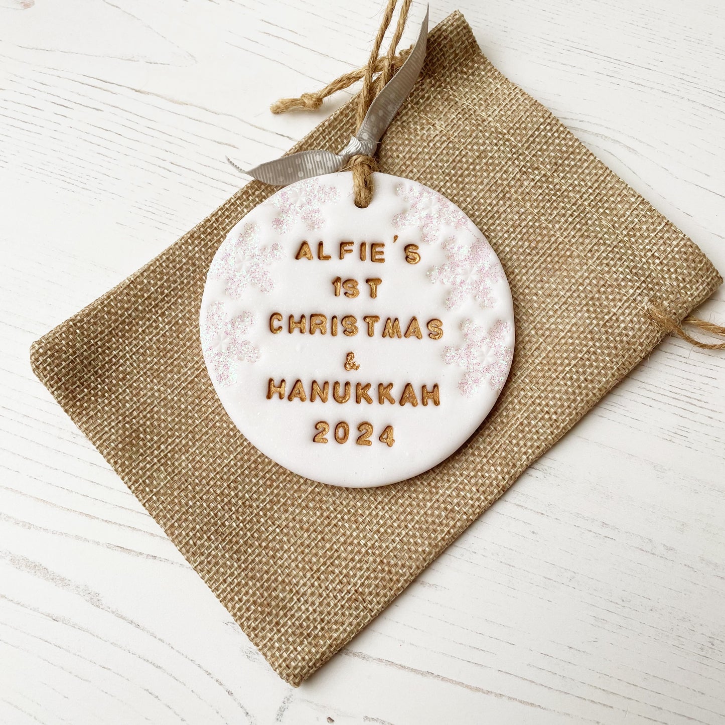 Personalised baby’s first Christmas and Hanukkah bauble ornament, glitter white clay round personalised with ALFIE’S FIRST CHRISTMAS & HANUKKAH 2024 in gold paint, decorated with 3 iridescent glitter snowflakes on either side of the bauble