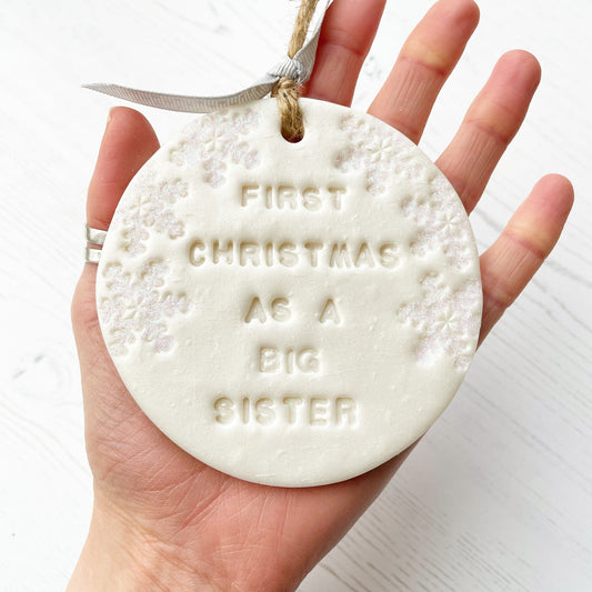 Personalised baby's first Christmas bauble ornament, pearlised white round clay with FIRST CHRISTMAS AS A BIG SISTER (letters not painted), decorated with 3 iridescent glitter snowflakes on either side of the bauble