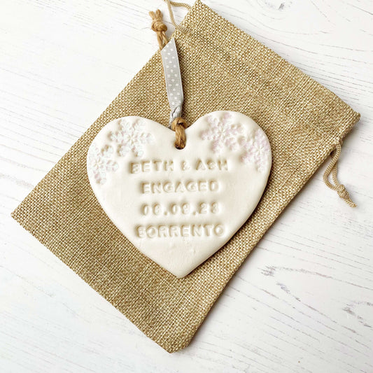 Personalised first Christmas engaged heart ornament, pearlised white clay with BETH & ASH ENGAGED 08.09.23 SORRENTO (text not painted), decorated with 2 iridescent glitter snowflakes on either side of the top of the heart