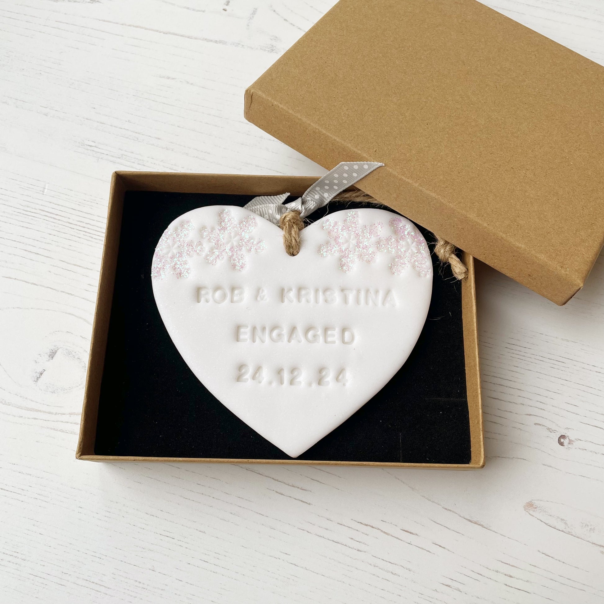 Personalised first Christmas engaged heart ornament, glitter white clay with ROB & KRISTINA ENGAGED 24.12.24 (text not painted), decorated with 2 iridescent glitter snowflakes on either side of the top of the heart