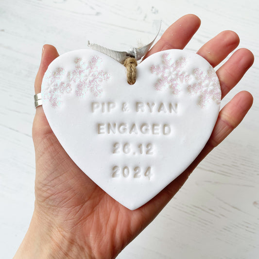 Personalised first Christmas engaged heart ornament, glitter white clay with PIP & RYAN ENGAGED 26.12 2024 (text not painted), decorated with 2 iridescent glitter snowflakes on either side of the top of the heart