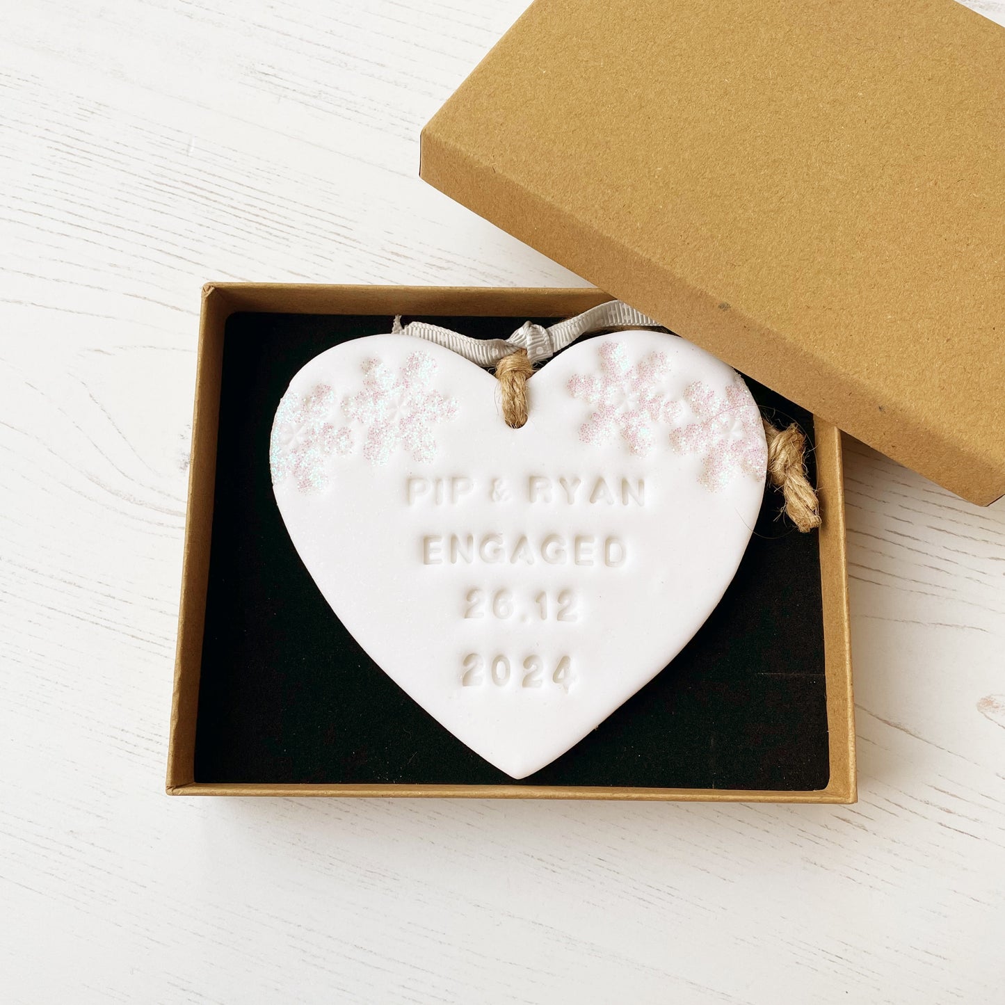 Personalised first Christmas engaged heart ornament, glitter white clay with PIP & RYAN ENGAGED 26.12 2024 (text not painted), decorated with 2 iridescent glitter snowflakes on either side of the top of the heart