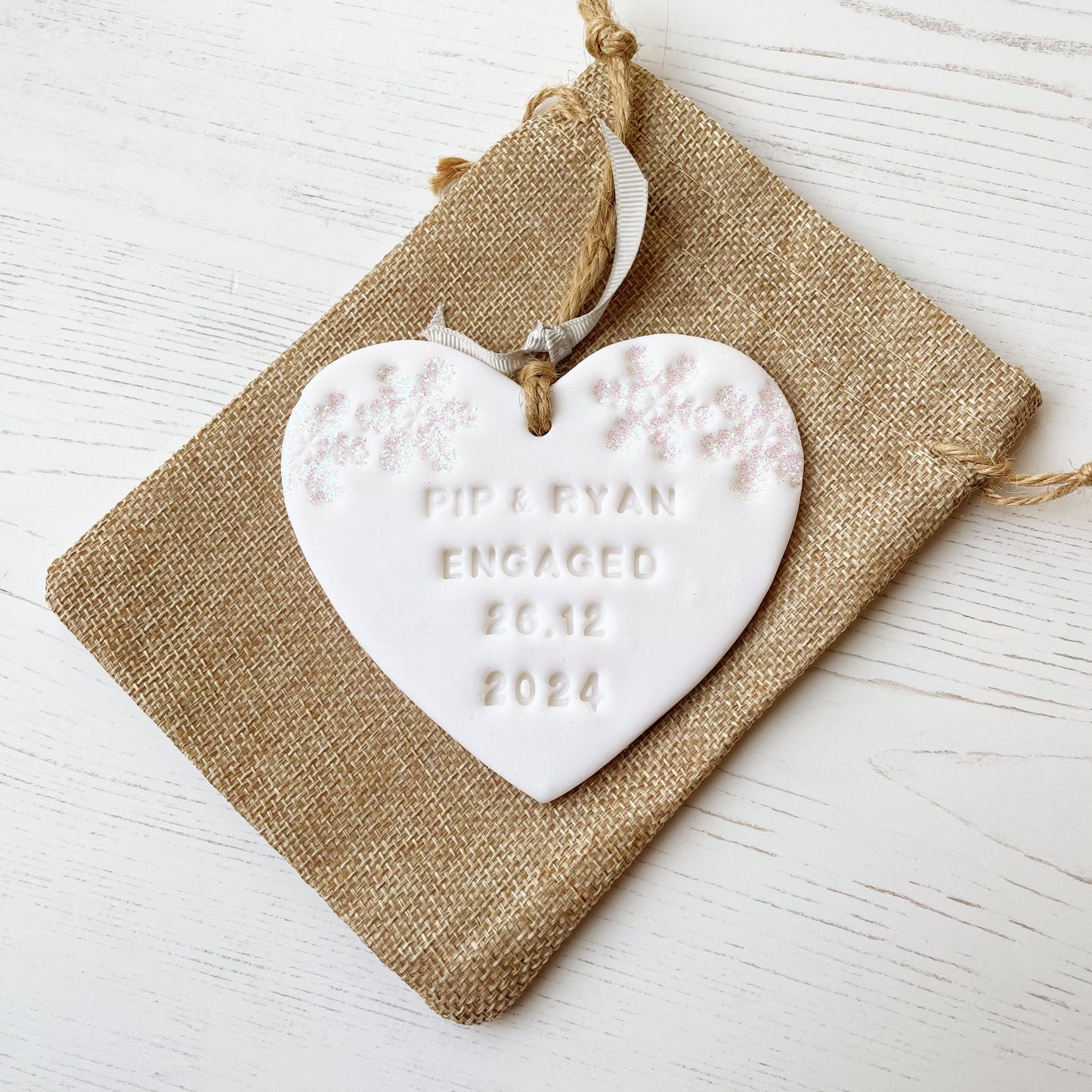 Personalised first Christmas engaged heart ornament, glitter white clay with PIP & RYAN ENGAGED 26.12 2024 (text not painted), decorated with 2 iridescent glitter snowflakes on either side of the top of the heart