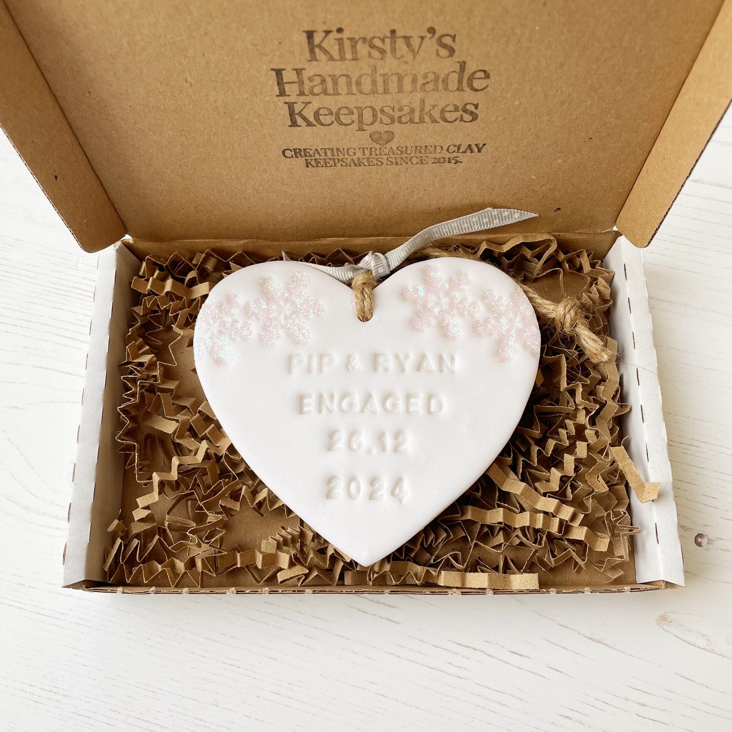 Personalised first Christmas engaged heart ornament, glitter white clay with PIP & RYAN ENGAGED 26.12 2024 (text not painted), decorated with 2 iridescent glitter snowflakes on either side of the top of the heart