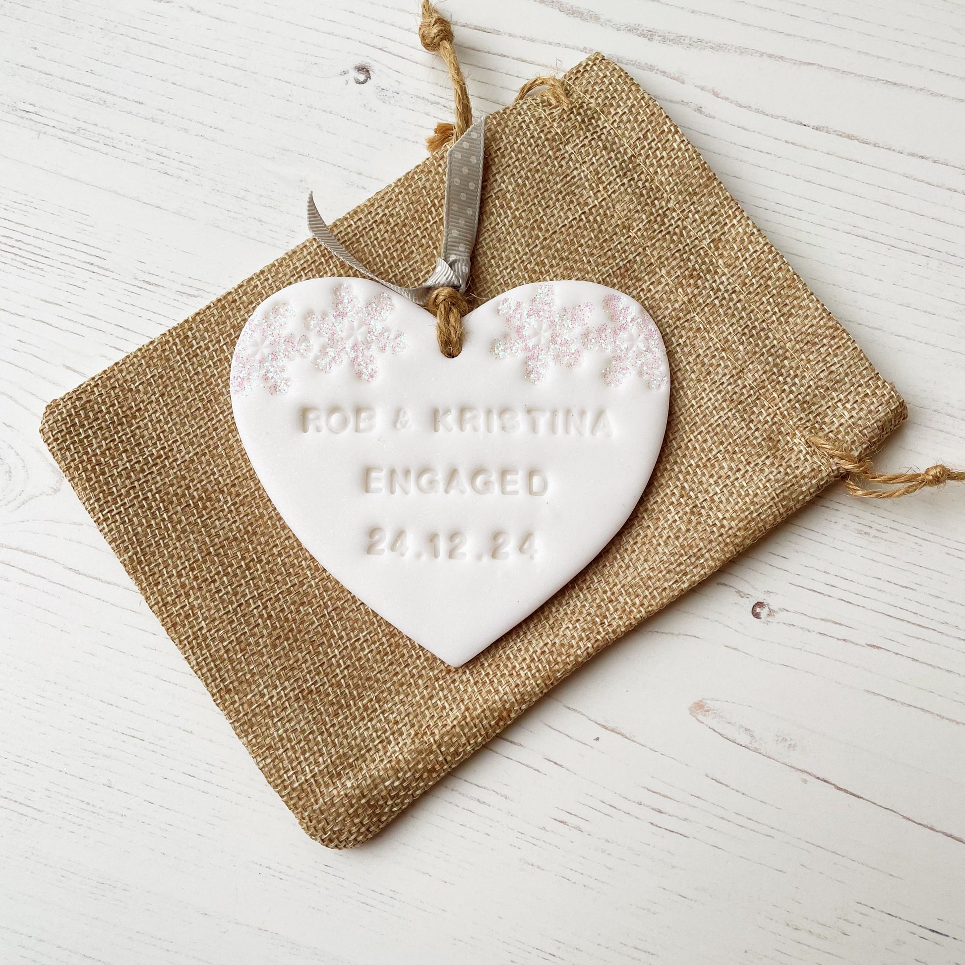 Personalised first Christmas engaged heart ornament, glitter white clay with ROB & KRISTINA ENGAGED 24.12.24 (text not painted), decorated with 2 iridescent glitter snowflakes on either side of the top of the heart
