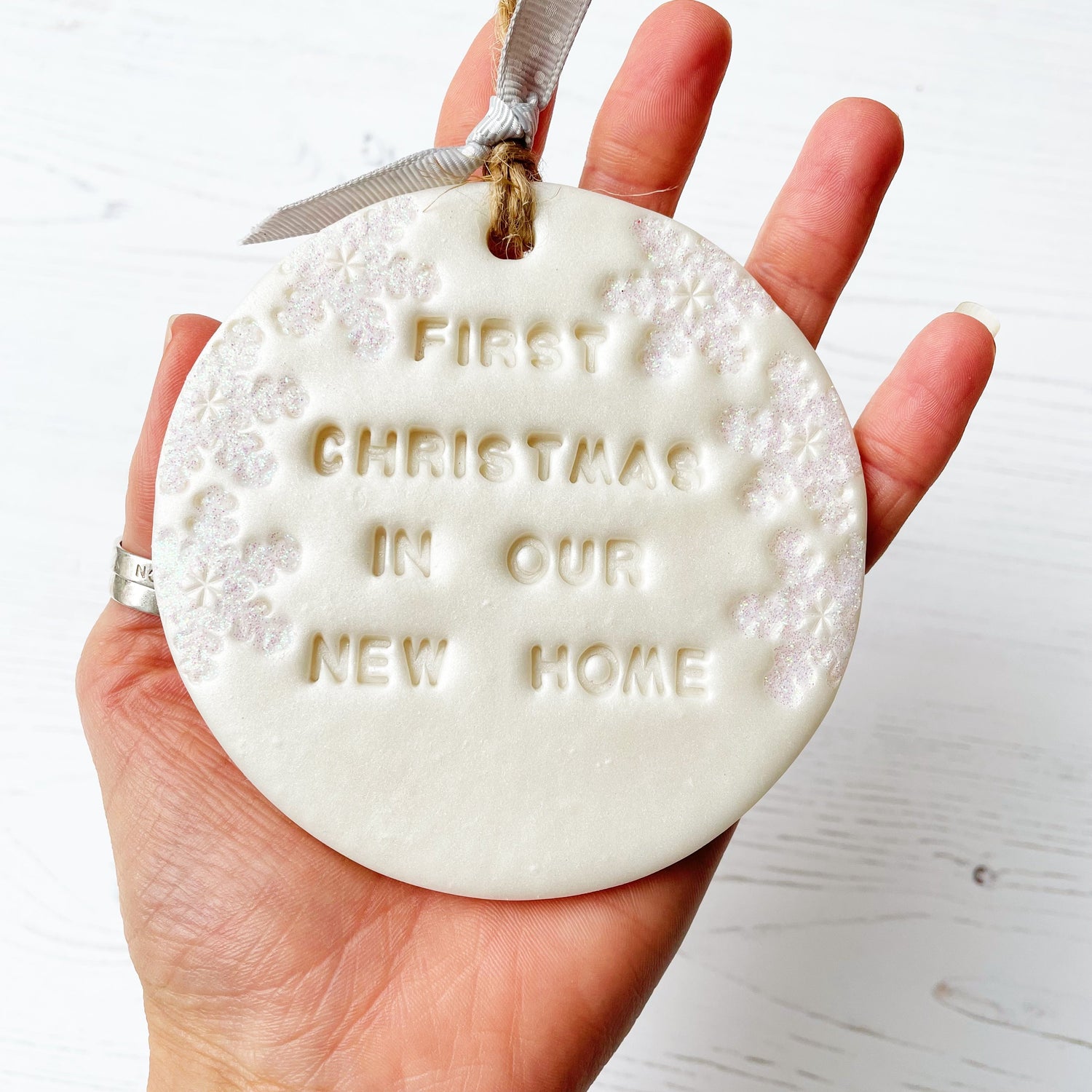 Personalised first Christmas in our new home bauble ornament, pearlised white round clay with FIRST CHRISTMAS IN OUR NEW HOME (text not painted), decorated with 3 iridescent glitter snowflakes on either side of the bauble