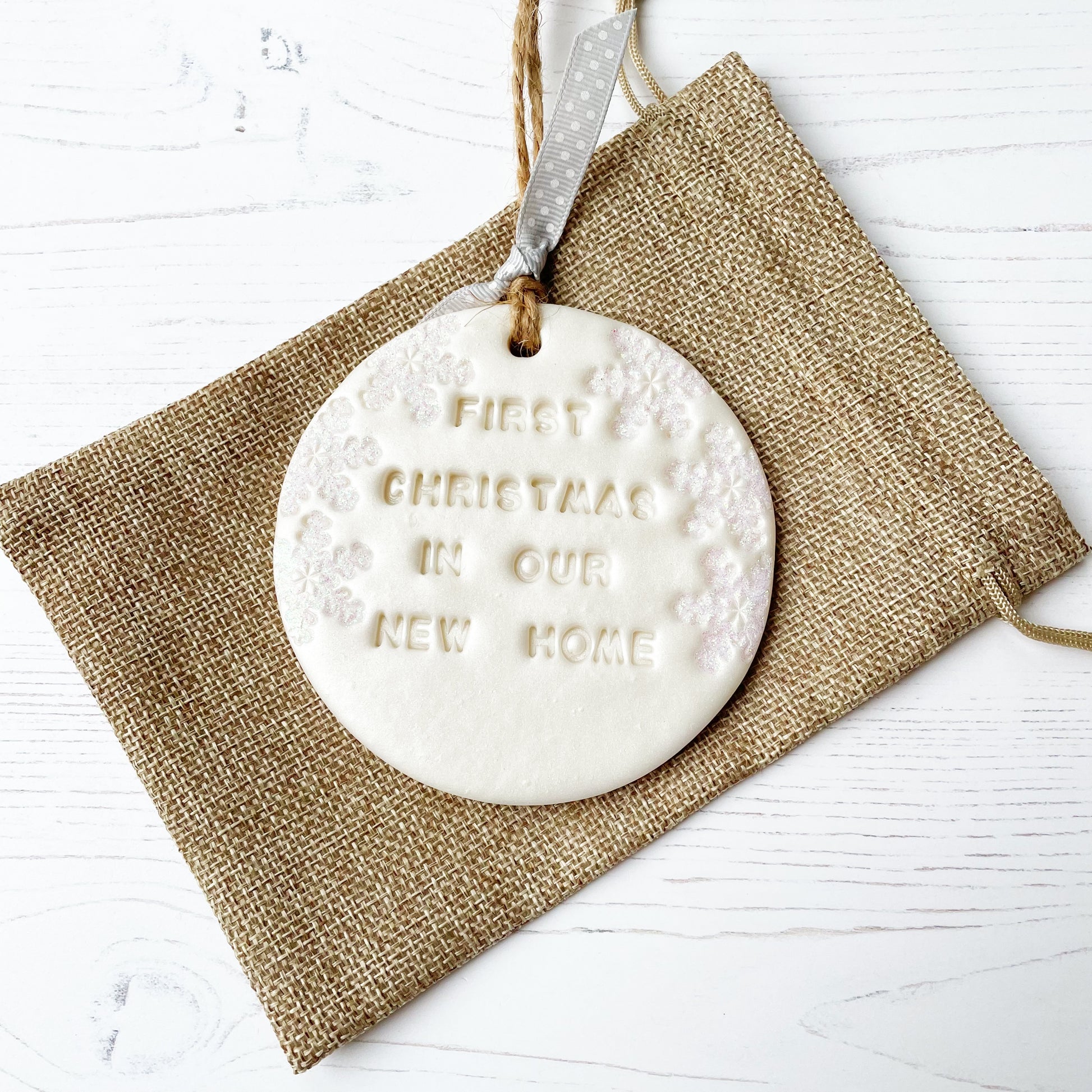Personalised first Christmas in our new home bauble ornament, pearlised white round clay with FIRST CHRISTMAS IN OUR NEW HOME (text not painted), decorated with 3 iridescent glitter snowflakes on either side of the bauble