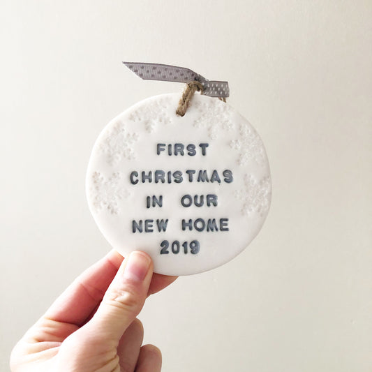 Personalised first Christmas in our new home bauble ornament, pearlised white clay round personalised with FIRST CHRISTMAS IN OUR NEW HOME 2019 in grey paint, decorated with 3 iridescent glitter snowflakes on either side of the bauble