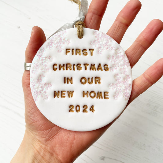 Personalised first Christmas in our new home bauble ornament, glitter white round clay with FIRST CHRISTMAS IN OUR NEW HOME 2024 painted in gold, decorated with 3 iridescent glitter snowflakes on either side of the bauble