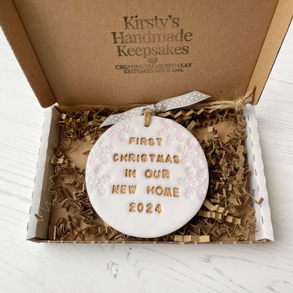 Personalised first Christmas in our new home bauble ornament, pearlised white round clay with FIRST CHRISTMAS IN OUR NEW HOME 2024 in gold, decorated with 3 iridescent glitter snowflakes on either side of the bauble
