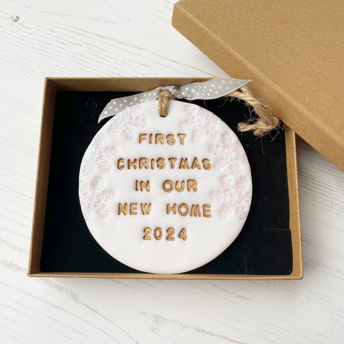 Personalised first Christmas in our new home bauble ornament, glitter white round clay with FIRST CHRISTMAS IN OUR NEW HOME 2024 painted in gold, decorated with 3 iridescent glitter snowflakes on either side of the bauble