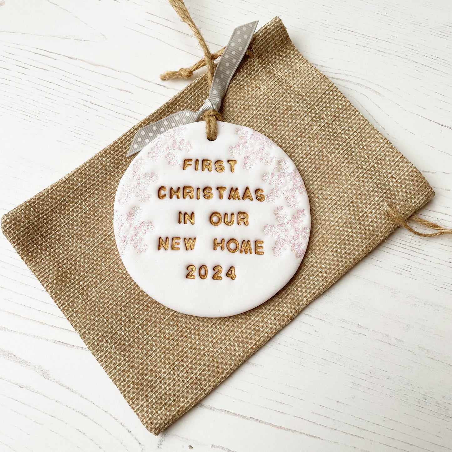 Personalised first Christmas in our new home bauble ornament, glitter white round clay with FIRST CHRISTMAS IN OUR NEW HOME 2024 painted in gold, decorated with 3 iridescent glitter snowflakes on either side of the bauble