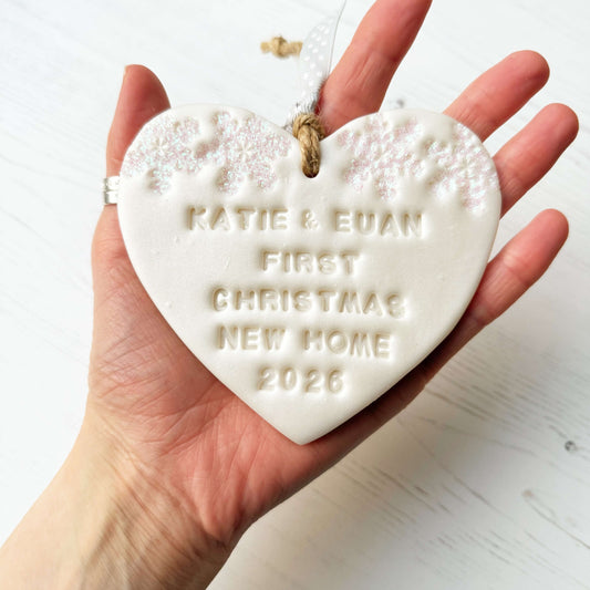 Personalised first Christmas new home heart ornament, Pearlised white polymer clay with KATIE & EUAN FIRST CHRISTMAS NEW HOME 2026 (text not painted), decorated with 2 iridescent glitter snowflakes on either side of the top of the heart