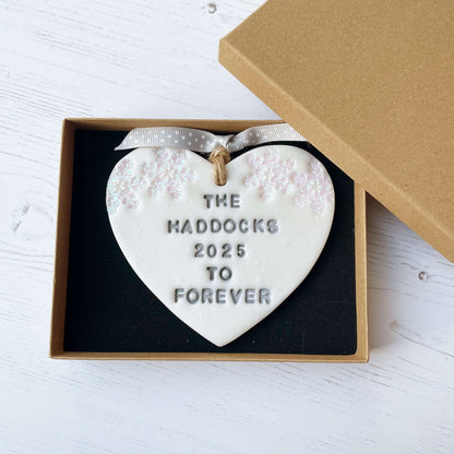 Personalised first Christmas married heart ornament, pearlised white clay personalised in grey with THE HADDOCKS 2025 TO FOREVER decorated with 2 iridescent glitter snowflakes on either side of the top of the heart